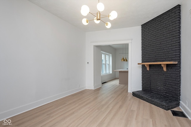 unfurnished living room featuring a textured ceiling, light hardwood / wood-style floors, a brick fireplace, and a notable chandelier