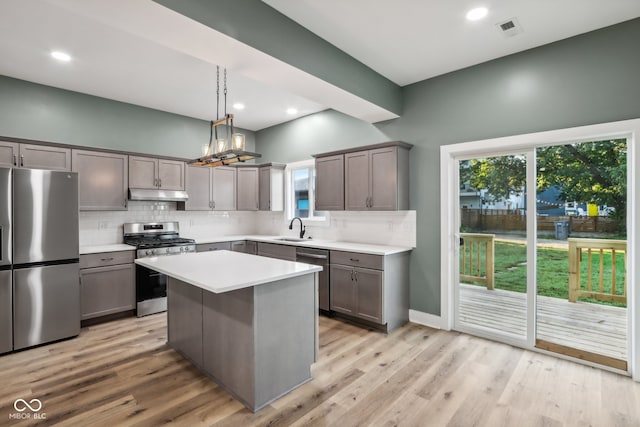 kitchen with pendant lighting, sink, a kitchen island, appliances with stainless steel finishes, and light wood-type flooring