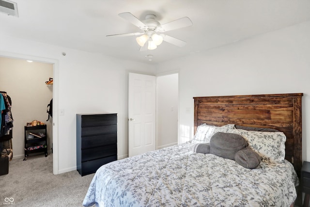 bedroom with a walk in closet, ceiling fan, and light colored carpet