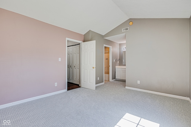 unfurnished bedroom featuring connected bathroom, light colored carpet, vaulted ceiling, and a closet