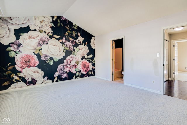 unfurnished bedroom featuring ensuite bathroom, wood-type flooring, and lofted ceiling