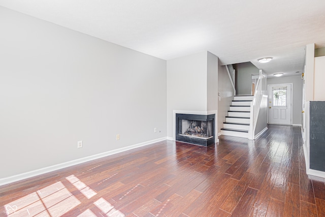 unfurnished living room featuring a multi sided fireplace and dark wood-type flooring