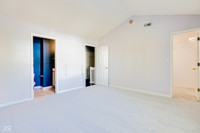 unfurnished bedroom featuring connected bathroom, a spacious closet, vaulted ceiling, light carpet, and a closet