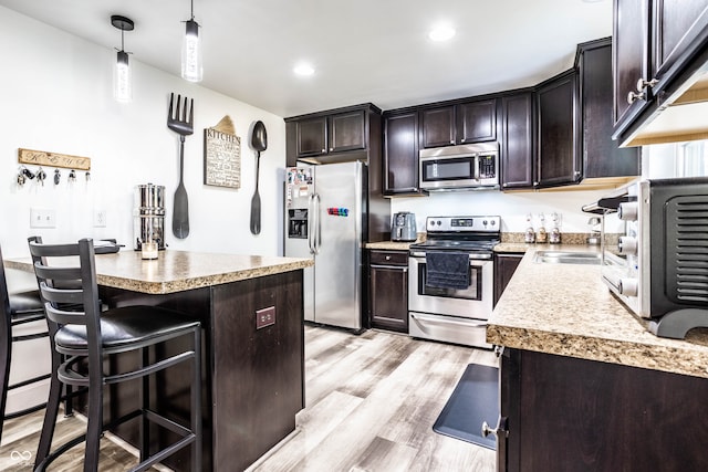 kitchen with sink, light wood-type flooring, decorative light fixtures, dark brown cabinetry, and stainless steel appliances