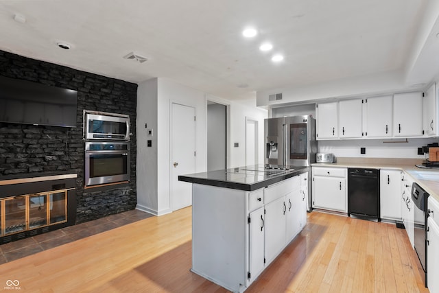 kitchen featuring appliances with stainless steel finishes, white cabinetry, a stone fireplace, light wood-type flooring, and a center island