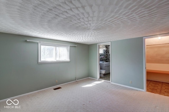 unfurnished bedroom with a textured ceiling, connected bathroom, carpet flooring, and a walk in closet