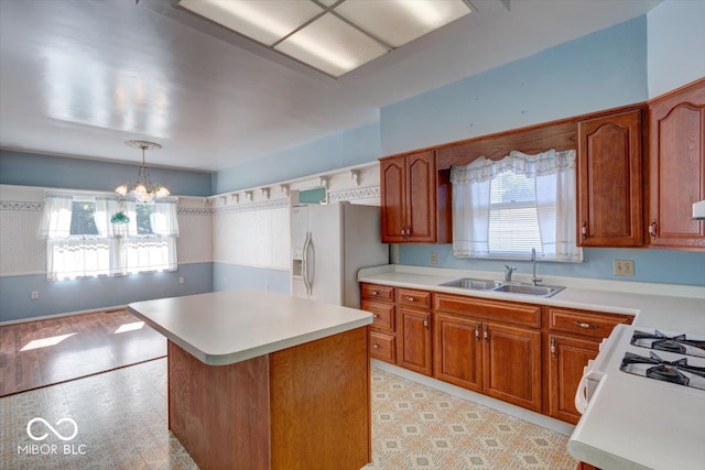 kitchen featuring a center island, sink, a notable chandelier, white appliances, and decorative light fixtures