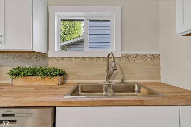 kitchen with sink, white cabinets, butcher block counters, decorative backsplash, and dishwashing machine