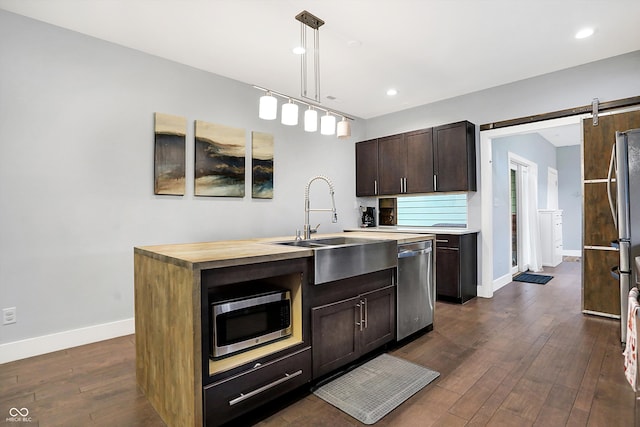 kitchen featuring dark wood-style floors, decorative light fixtures, a barn door, appliances with stainless steel finishes, and baseboards