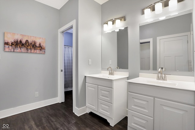 full bathroom featuring two vanities, a sink, baseboards, and wood finished floors