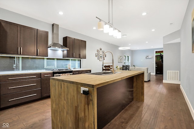 kitchen featuring visible vents, butcher block countertops, wall chimney range hood, stainless steel range with gas cooktop, and a sink