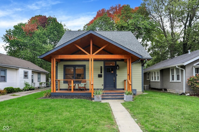 view of front of house with covered porch, a shingled roof, and a front yard