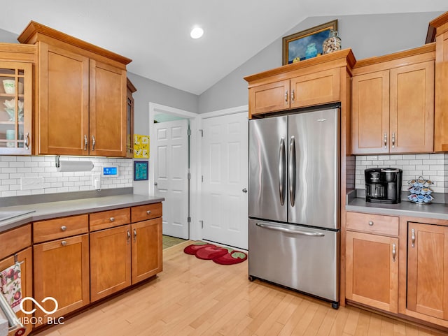 kitchen featuring vaulted ceiling, light hardwood / wood-style floors, tasteful backsplash, and stainless steel fridge