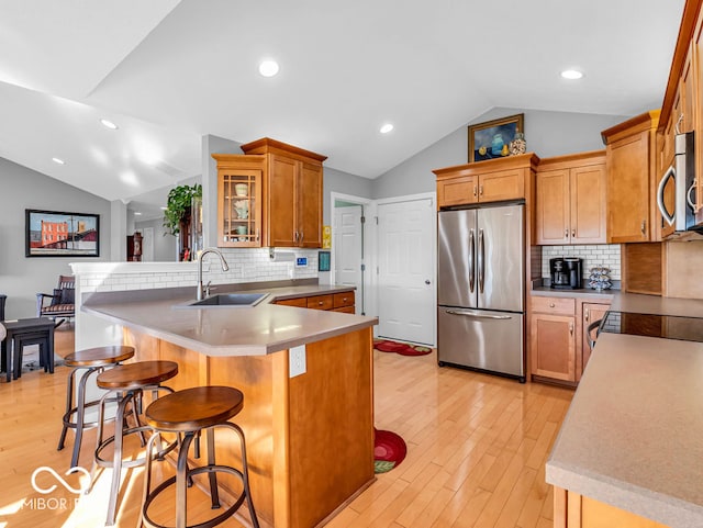 kitchen with vaulted ceiling, a breakfast bar, kitchen peninsula, stainless steel appliances, and light wood-type flooring