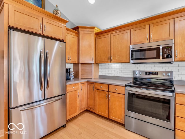 kitchen with appliances with stainless steel finishes, decorative backsplash, light hardwood / wood-style floors, and lofted ceiling