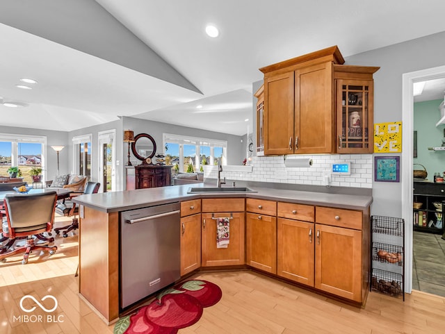 kitchen featuring vaulted ceiling, kitchen peninsula, light hardwood / wood-style flooring, stainless steel dishwasher, and sink