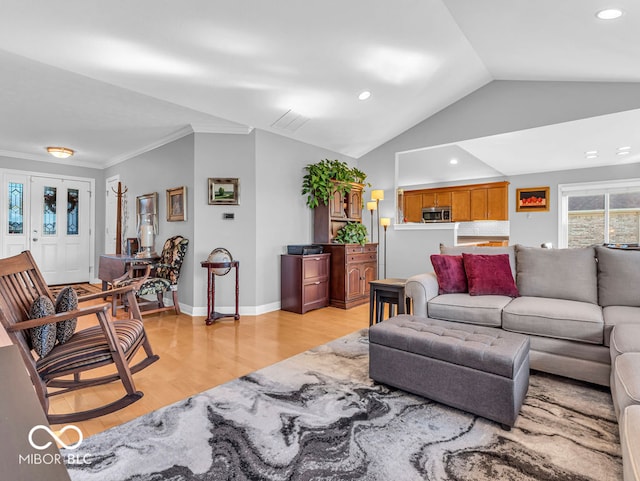 living room with light wood-type flooring, ornamental molding, and vaulted ceiling