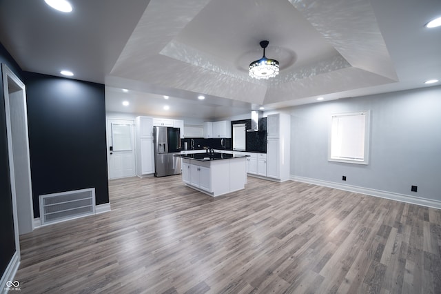 kitchen with white cabinets, a raised ceiling, a kitchen island with sink, and stainless steel fridge