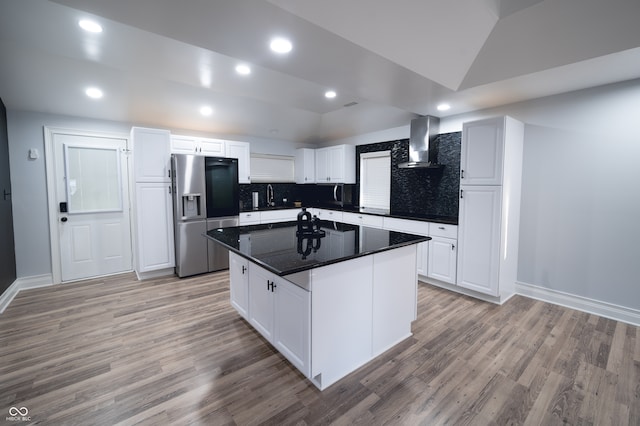 kitchen with white cabinets, stainless steel refrigerator with ice dispenser, wall chimney exhaust hood, and a kitchen island