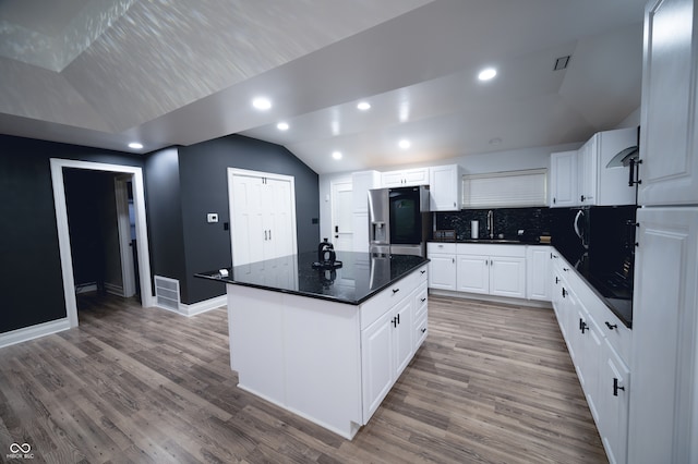 kitchen featuring lofted ceiling, a center island, stainless steel fridge, and white cabinetry