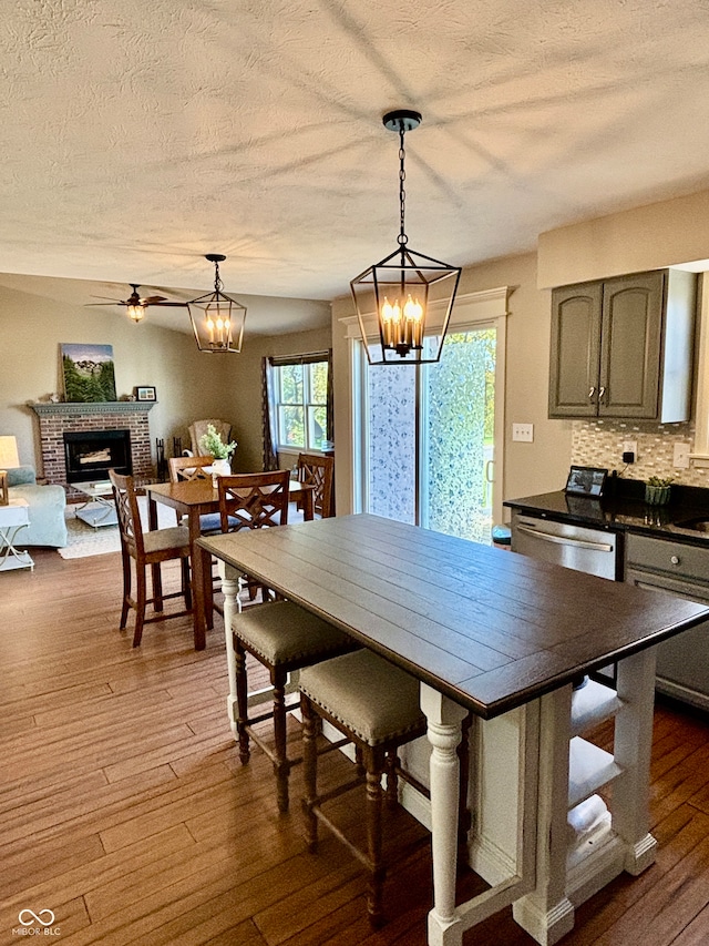 dining area with a textured ceiling, ceiling fan with notable chandelier, dark hardwood / wood-style flooring, and a fireplace