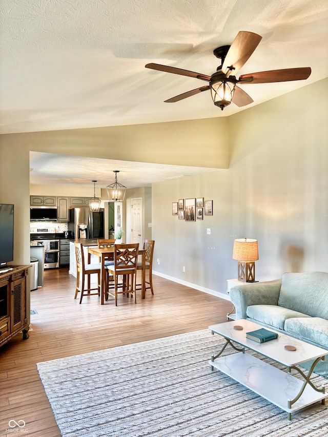 living room with a textured ceiling, light hardwood / wood-style floors, vaulted ceiling, and ceiling fan