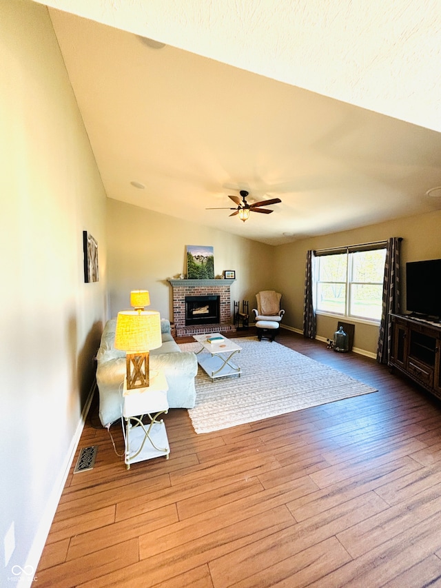 living room featuring hardwood / wood-style flooring, ceiling fan, and a brick fireplace