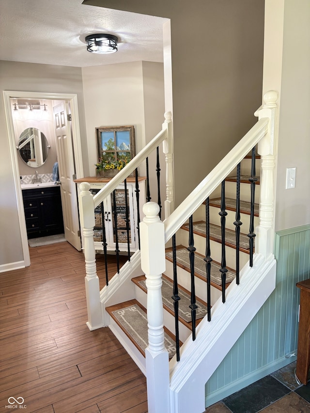 stairs featuring wood-type flooring, a textured ceiling, wood walls, and sink