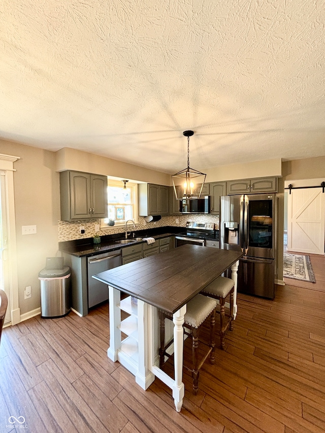 kitchen with sink, a barn door, wood-type flooring, decorative light fixtures, and appliances with stainless steel finishes