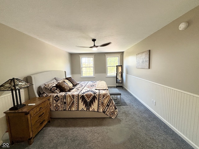 bedroom featuring dark colored carpet, ceiling fan, wood walls, and a textured ceiling