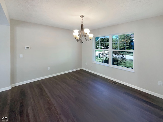 spare room with an inviting chandelier, dark hardwood / wood-style flooring, and a textured ceiling