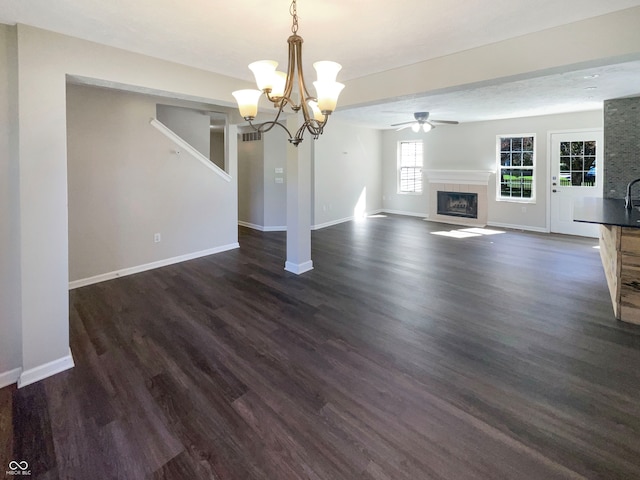 unfurnished living room with a textured ceiling, ceiling fan with notable chandelier, and dark hardwood / wood-style flooring