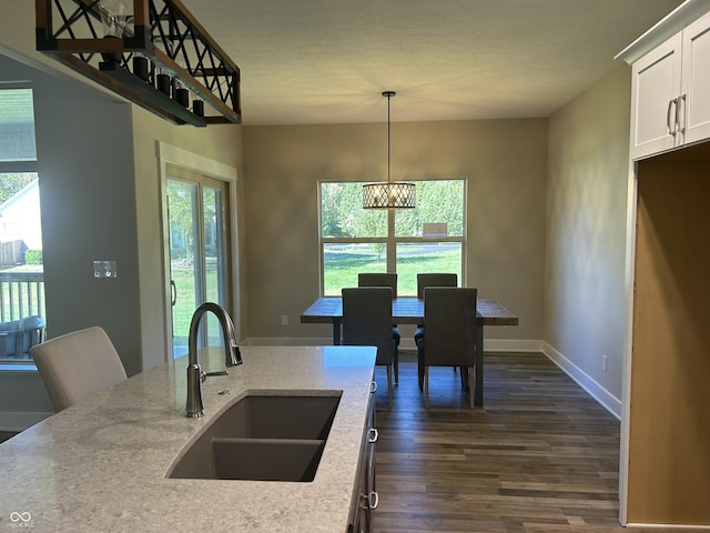 kitchen with pendant lighting, dark wood finished floors, white cabinets, a chandelier, and a sink