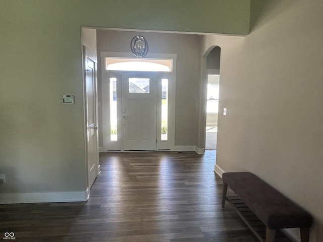 entryway featuring arched walkways, baseboards, and dark wood finished floors