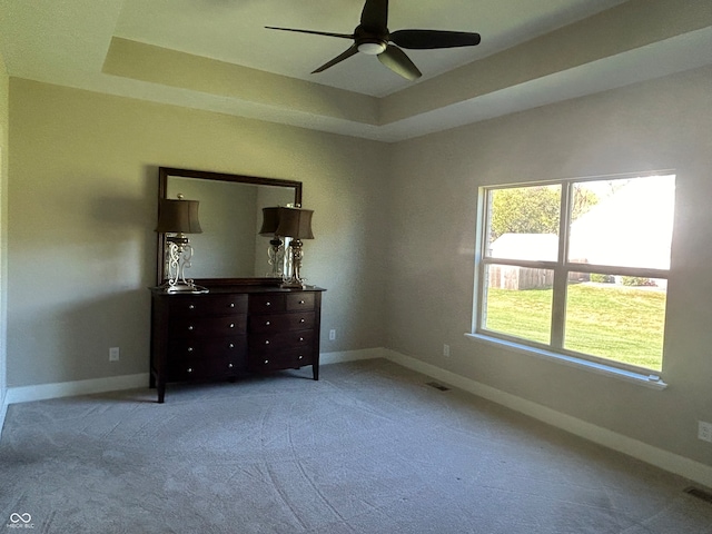 unfurnished bedroom featuring a tray ceiling, light carpet, and ceiling fan