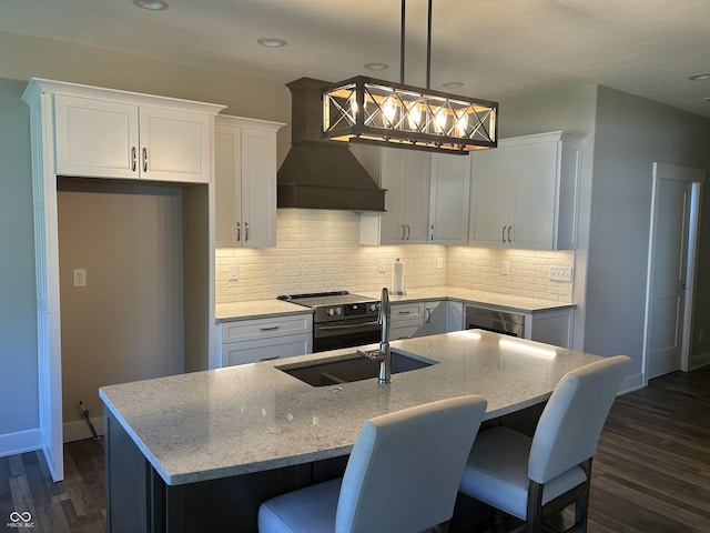 kitchen featuring a sink, an island with sink, premium range hood, electric stove, and dark wood-style floors