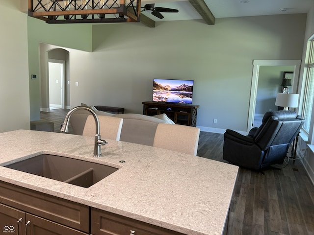 kitchen with beamed ceiling, arched walkways, dark wood-style flooring, a sink, and open floor plan