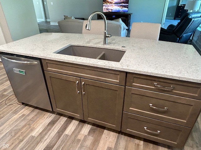 kitchen with light hardwood / wood-style floors, stainless steel dishwasher, light stone counters, and sink