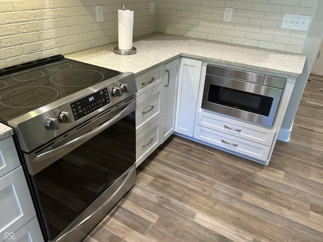 kitchen with tasteful backsplash, dark wood finished floors, white cabinetry, light stone countertops, and stainless steel appliances