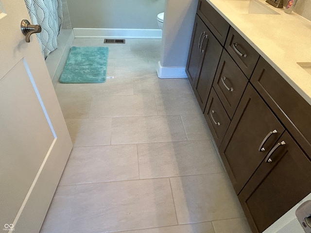 bathroom with walk in shower, vanity, tile patterned flooring, and toilet