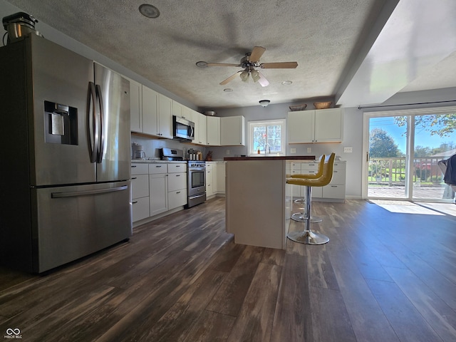 kitchen with white cabinets, dark hardwood / wood-style flooring, a kitchen breakfast bar, a kitchen island, and stainless steel appliances