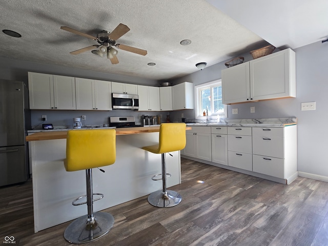 kitchen with a kitchen island, dark wood-type flooring, a breakfast bar, white cabinetry, and appliances with stainless steel finishes