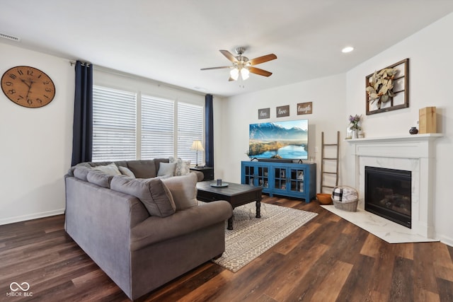 living room with a high end fireplace, ceiling fan, and dark wood-type flooring