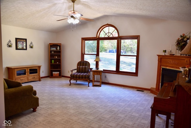 sitting room with a ceiling fan, a textured ceiling, a fireplace with raised hearth, light colored carpet, and lofted ceiling
