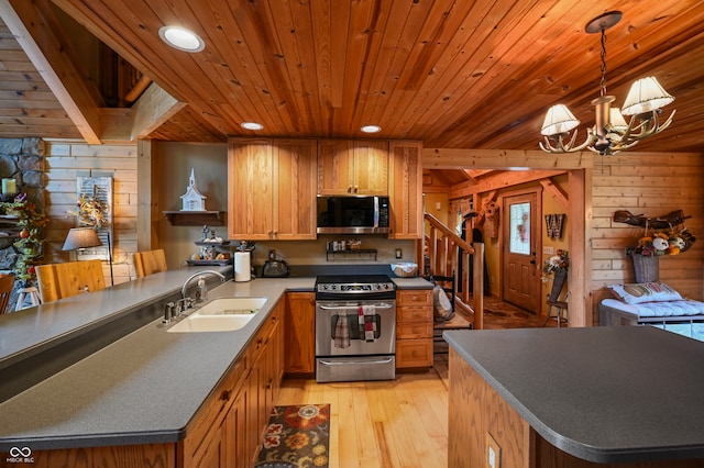 kitchen with pendant lighting, stainless steel appliances, wood walls, and sink