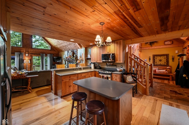 kitchen featuring light wood-type flooring, vaulted ceiling, kitchen peninsula, hanging light fixtures, and appliances with stainless steel finishes