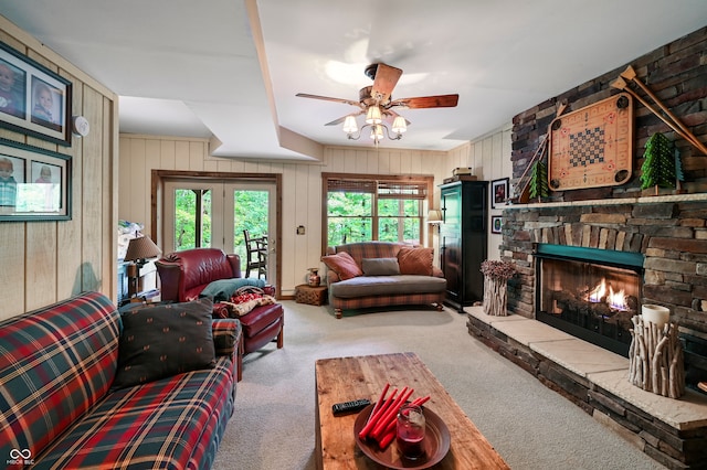 living room featuring wood walls, ceiling fan, light colored carpet, and a fireplace