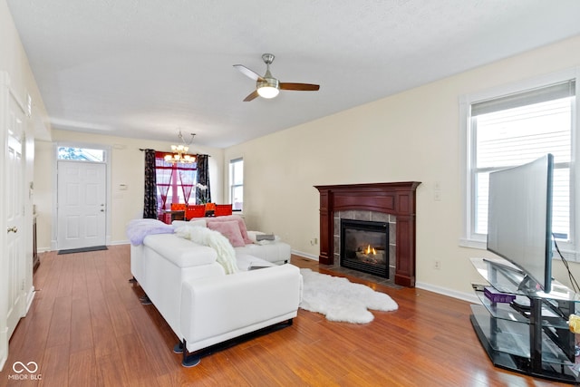 living room featuring ceiling fan with notable chandelier, a tiled fireplace, a wealth of natural light, and hardwood / wood-style floors