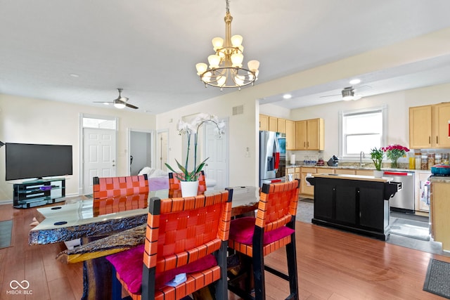 dining area with ceiling fan with notable chandelier, sink, and light hardwood / wood-style flooring