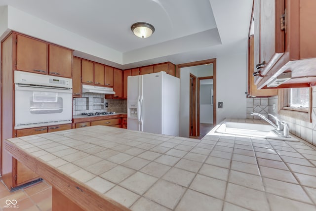 kitchen featuring tile countertops, kitchen peninsula, backsplash, sink, and white appliances